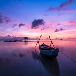A boat on the calm see with a beautiful background of pink and blue colors.