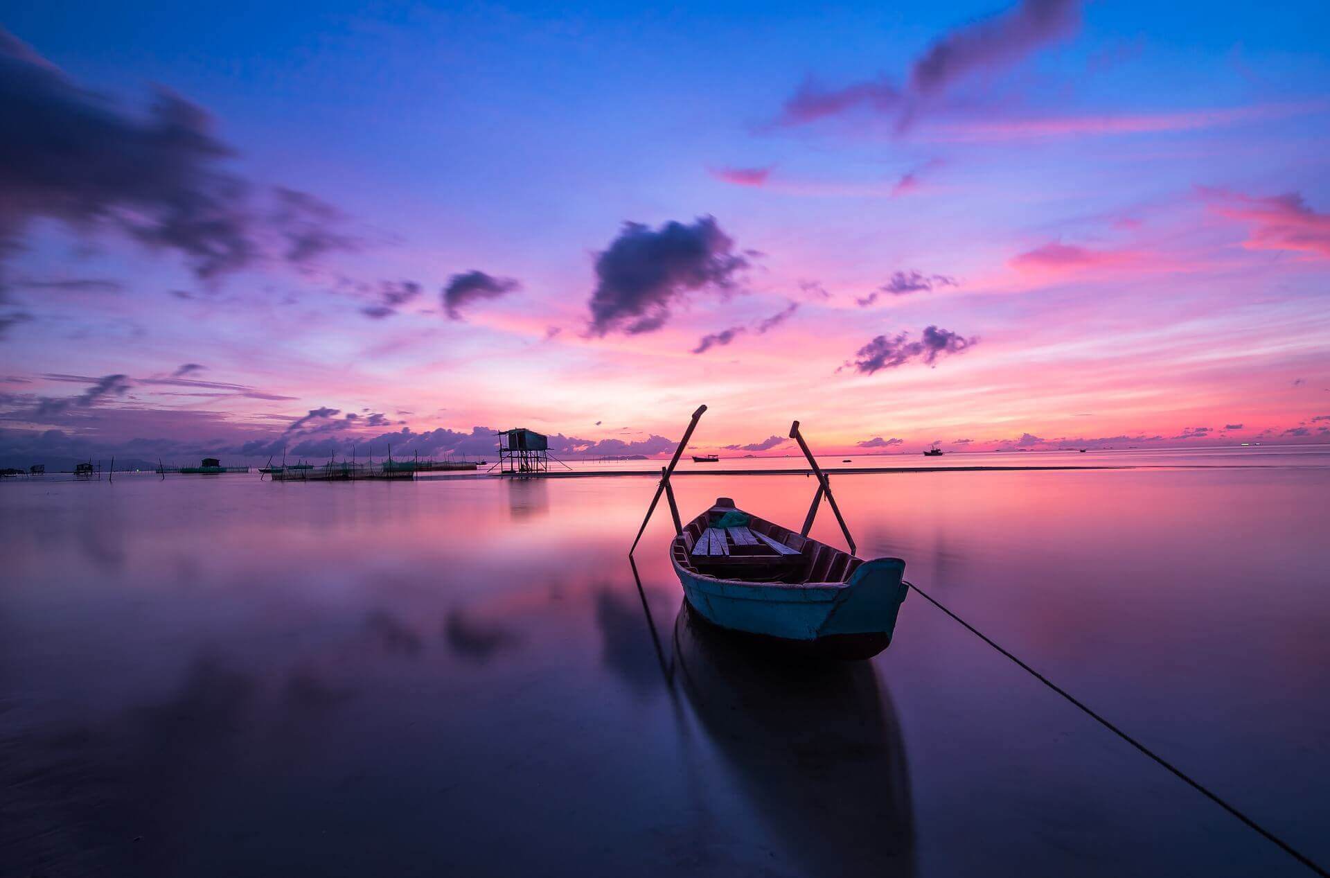 A boat on the calm see with a beautiful background of pink and blue colors.