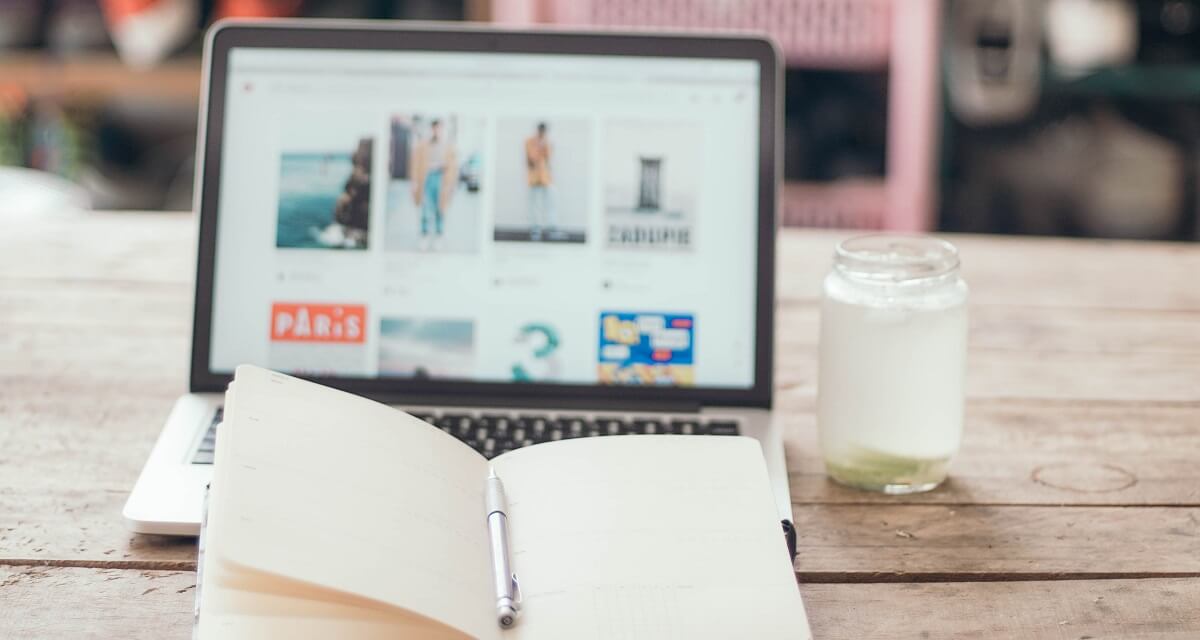 An open notebook and a MacBook on a wooden desk.