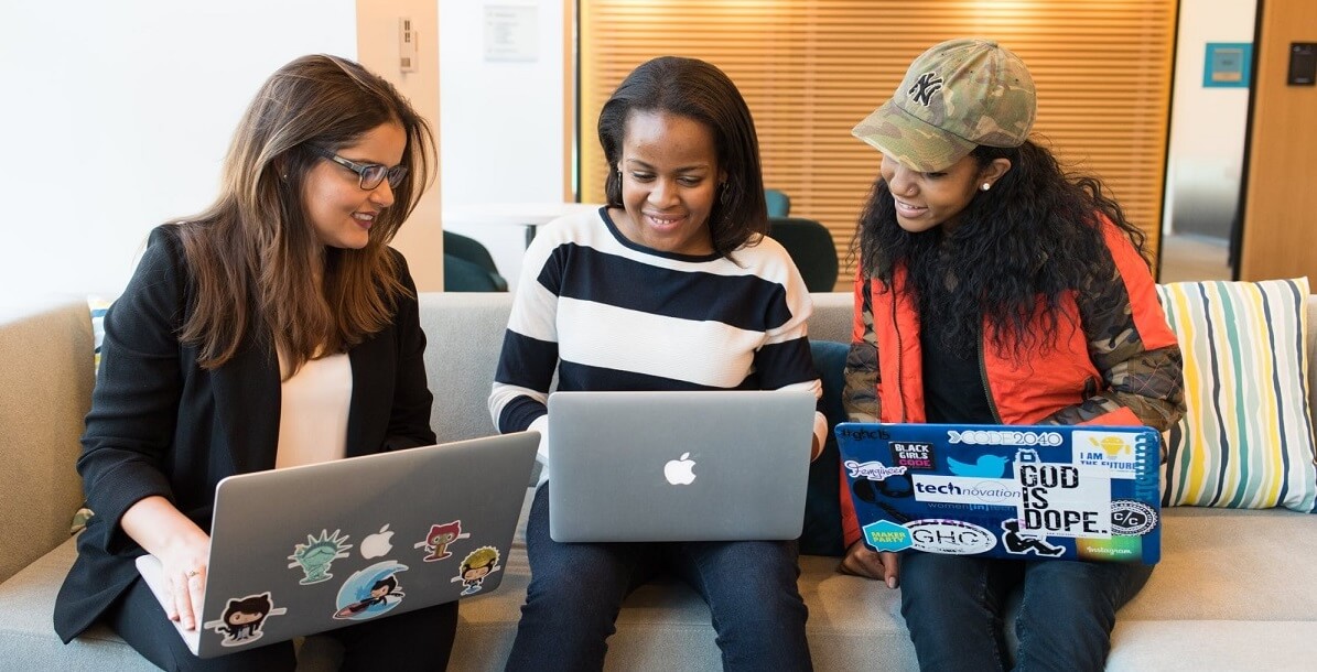 Three women sitting on a couch, working on their laptops.