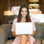 A young woman sitting on a sofa, working on a laptop.