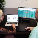 A man and a woman discussing business issues in front of their computers.