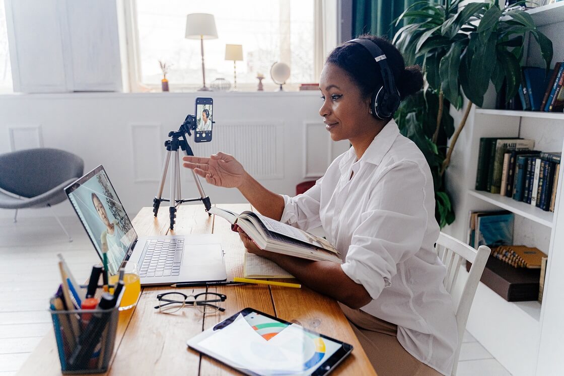 black woman infront of a laptop teaching with a book