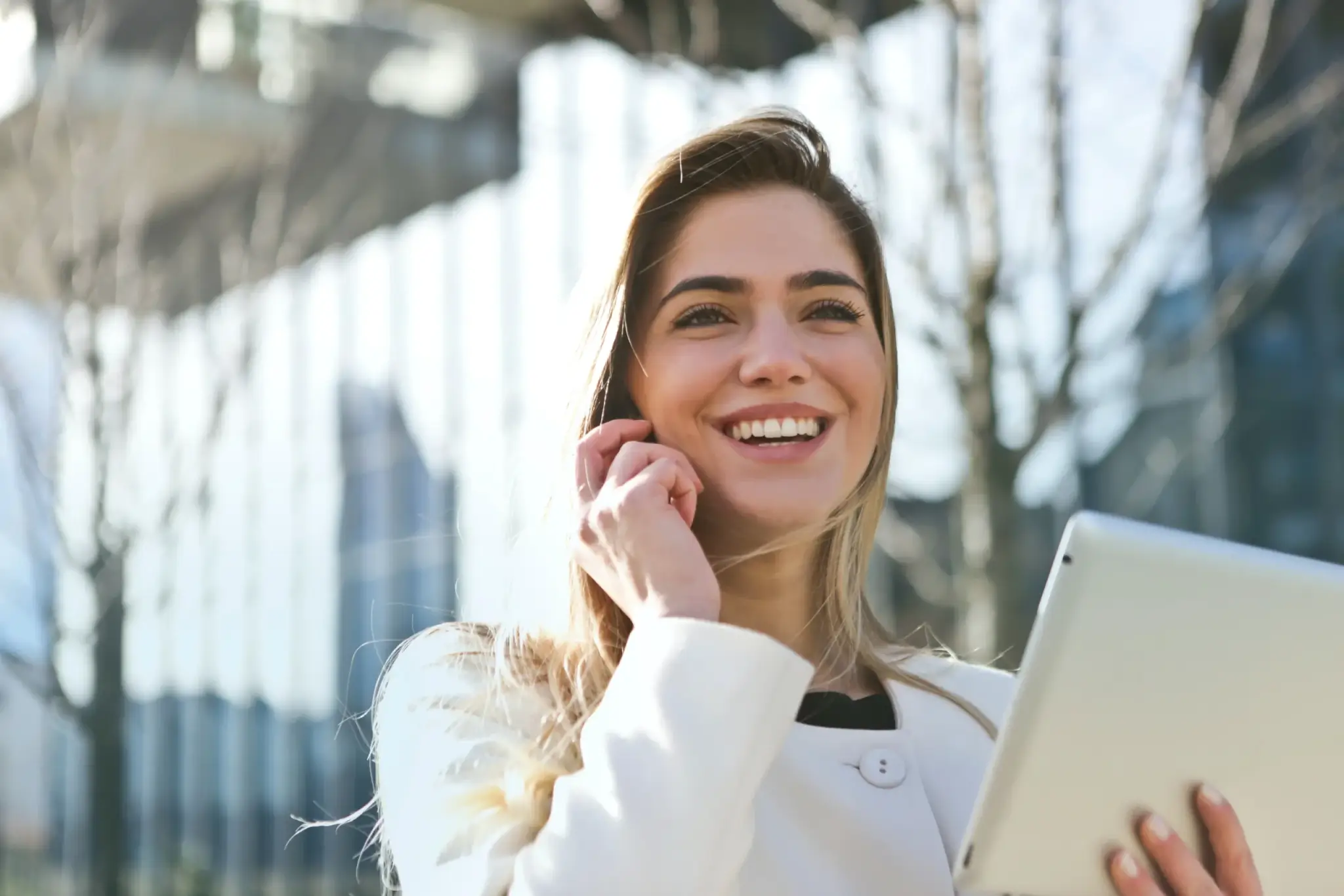 A smiling woman talking on the phone while holding a tablet.