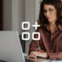 An image showing a woman with wavy hair and glasses useing a laptop.