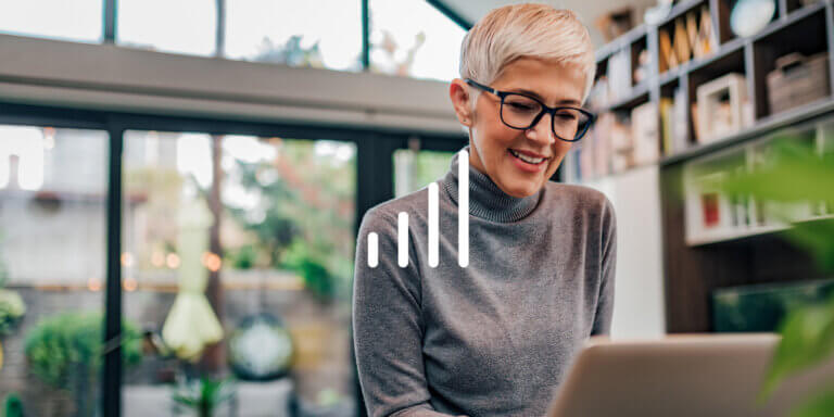 A woman with short blond hair smiling while looking at a laptop screen.