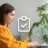 A visual showing a girl with long brown hair and wearing an orange sweater typing something on a laptop screen.