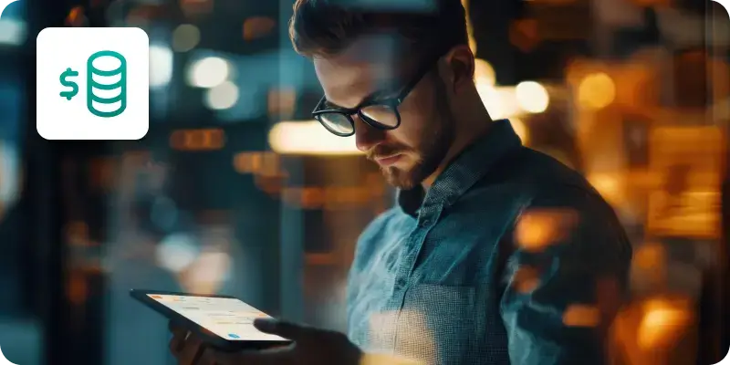 An image showing a man wearing glasses holding and looking at a tablet.