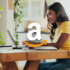 An image showing a girl with long black hair and wearing a yellow shirt using a laptop with an amazon logo in the centre.