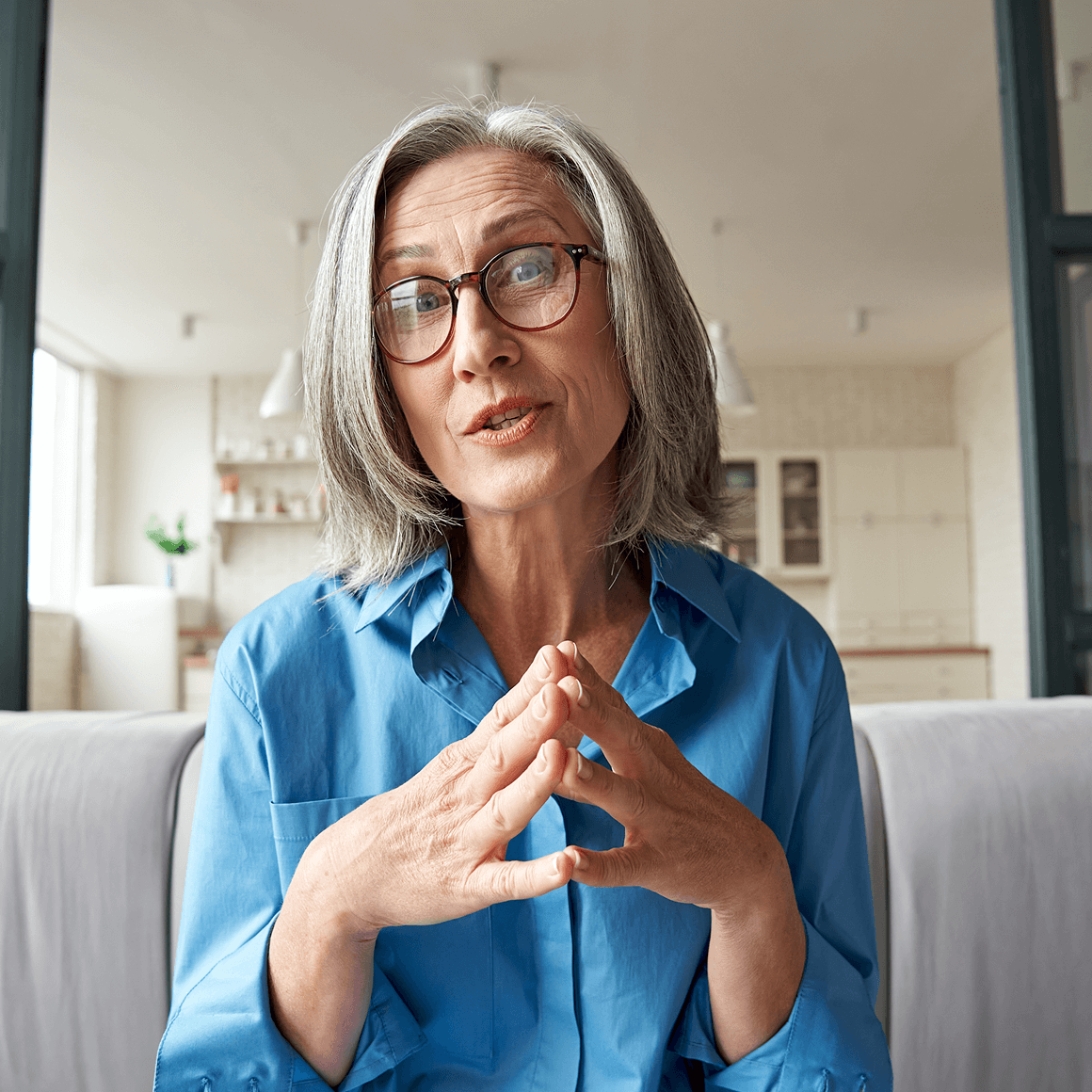Woman speaking directly to the camera with her hands clasped.