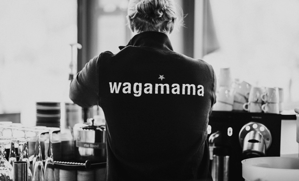 Restaurant employee wearing a Wagamama uniform while working behind a counter in a café or restaurant environment.